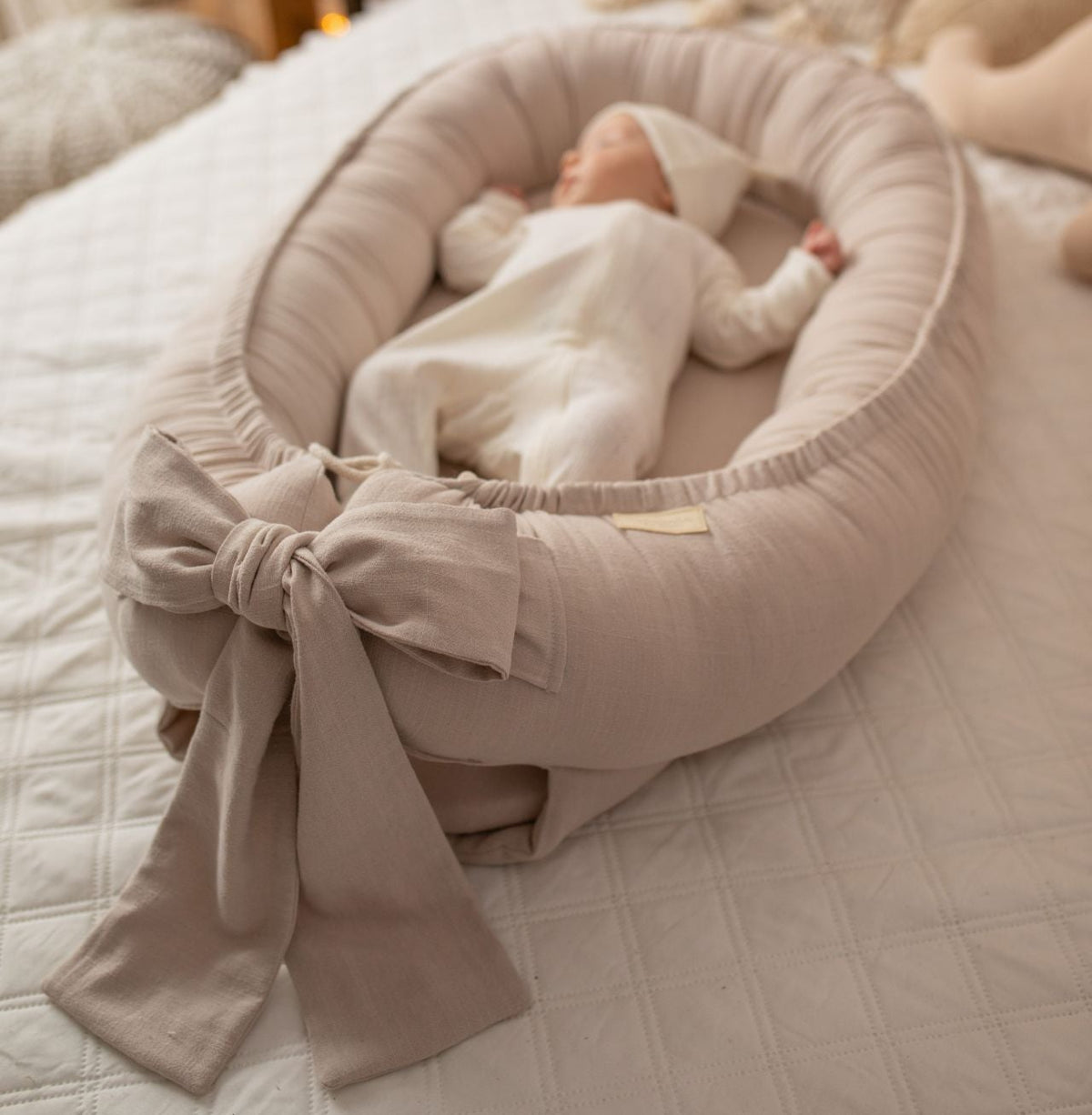 Newborn baby in a beige baby nest on a bed with soft lighting and decor.
