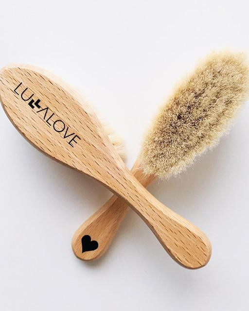 Two baby hairbrushes with wooden handles, one with stiff bristles for cradle cap and one with soft bristles for gentle use.